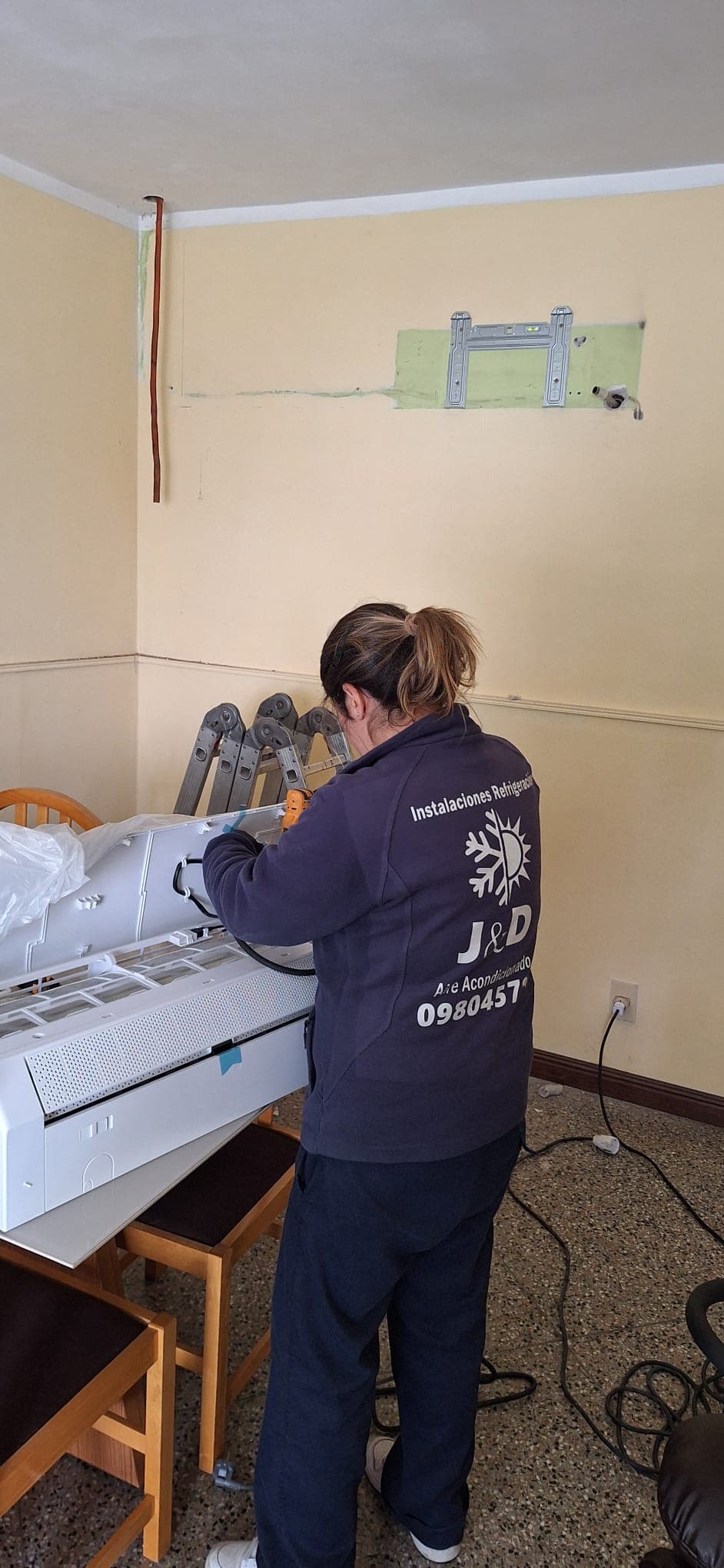 Integrante del equipo de J&D, con la campera de la empresa, preparando la unidad interior de un split sobre una mesa, con el soporte ya montado en la pared.