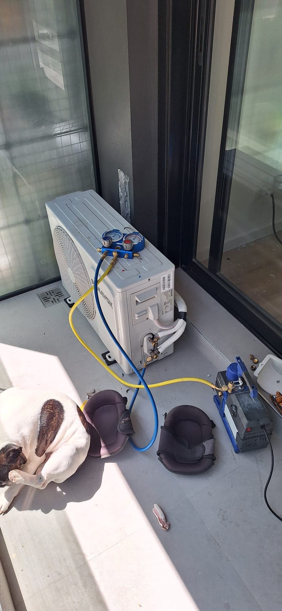 Unidad exterior en un balcón durante el vacío del sistema, con el manómetro y la bomba de vacío conectados.